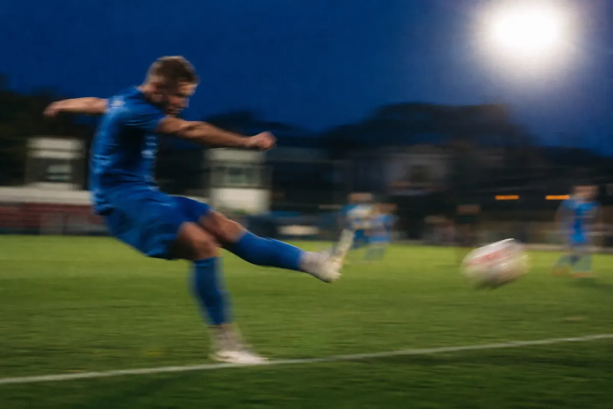 Bewegungsunscharfe Aufnahme eines Spielers im blauen Trikot beim Torschuss unter Flutlicht