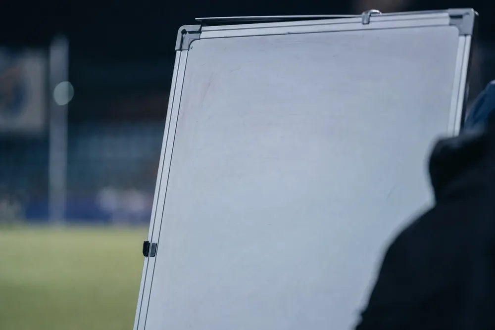 Leeres Flipchart am Spielfeldrand, dahinter unscharf Rasen und Tribüne